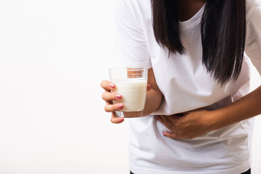 Mujer sosteniendo un vaso de leche pone su mano en estomago por el dolor