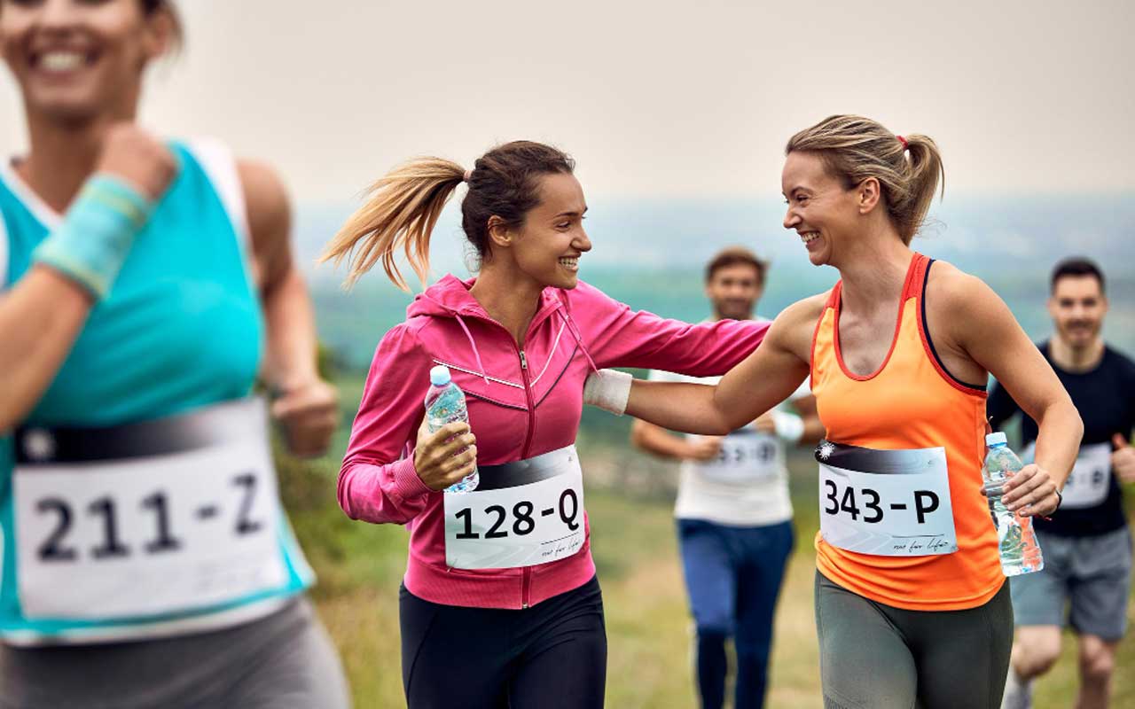 Mujeres atléticas felices apoyándose mutuamente mientras corren un maratón en la naturaleza
